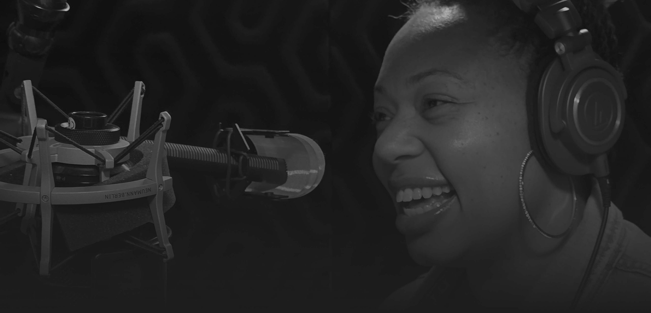 A person wearing headphones speaks into a microphone in a recording studio.