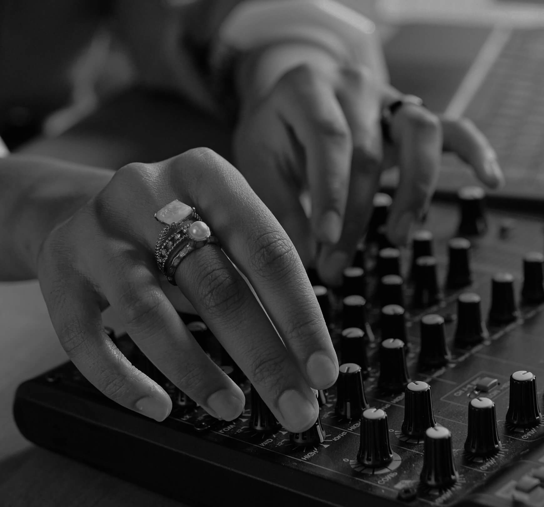 A close-up of two hands adjusting knobs on an audio mixing console, with rings visible on the fingers.