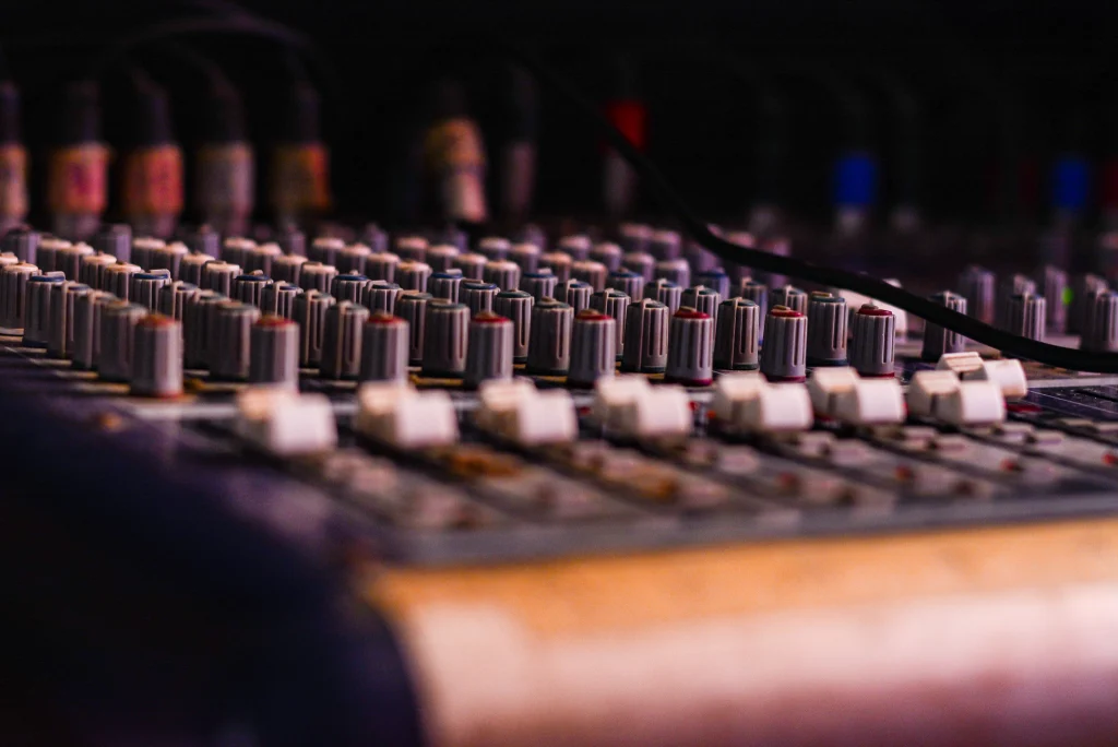 A close-up of an audio mixing console used to record hip hop politics, showing rows of knobs and sliders.